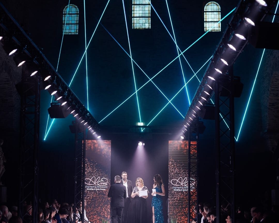 Grande salle en lumière de soirée, scène et tables, vue depuis le fond